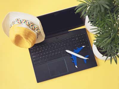 A laptop with a hat and a plant on a yellow background.