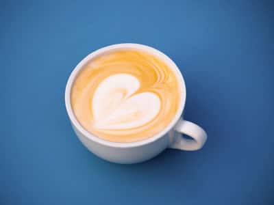 A cup of coffee with heart-shaped latte art on a blue background.