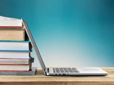 A laptop lies in front of a stack of books.