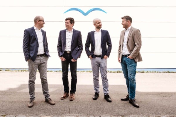 Four men stand in front of a white building with the Bluebird logo over their head.