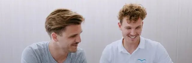 Zwei junge BLUEBIRD-Berater lachen gemeinsam am Laptop